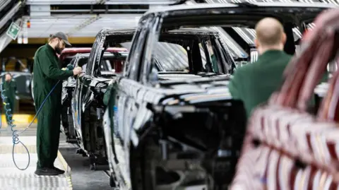 Getty Images An employee where dark green overalls and a cap polishes paint on the bodywork of a Range Rover sports utility vehicle (SUV) in the paint shop at Jaguar Land Rover vehicle manufacturing plant in Solihull, UK.