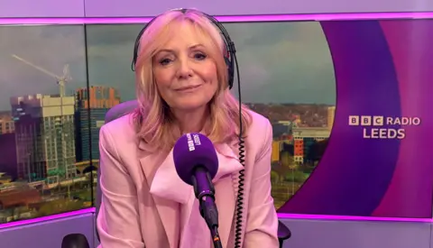 BBC Image shows the mayor of West Yorkshire wearing a pale pink suit speaking into a BBC Radio Leeds microphone. She has headphones on and is sitting in front of an image of Leeds.